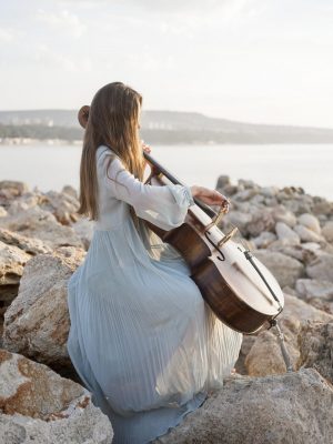vue-laterale-du-musicien-jouant-du-violoncelle-sur-les-rochers-au-bord-de-la-mer